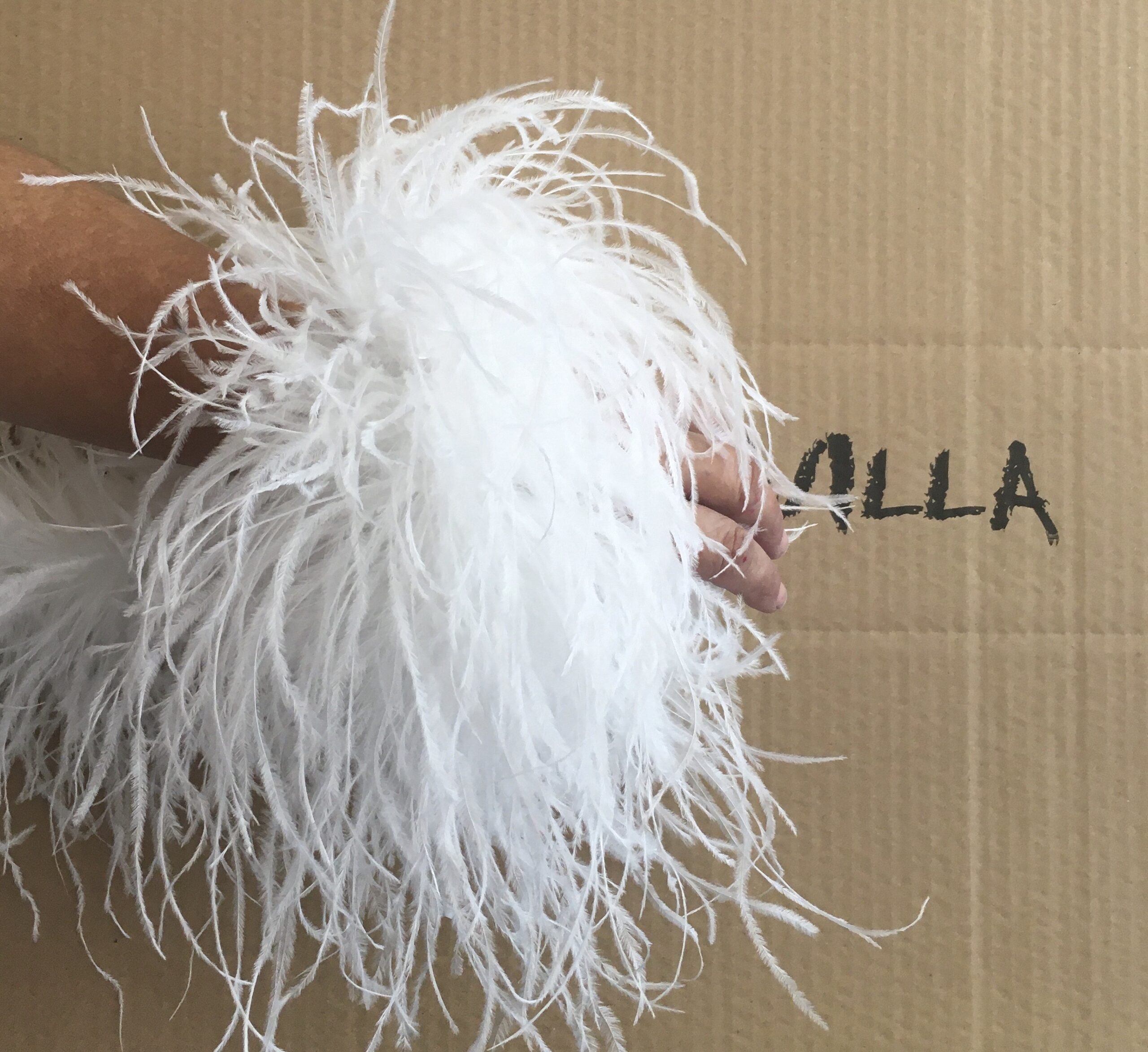 Pareja de puños de plumas de avestruz naturales y desmontables colocados sobre las mangas de un vestido de invitada.