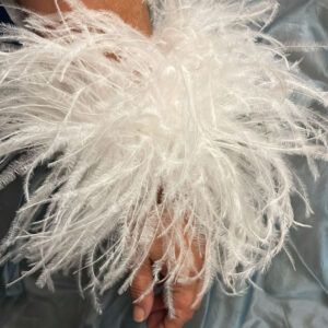 Pareja de puños de plumas de avestruz naturales y desmontables colocados sobre las mangas de un vestido de invitada.