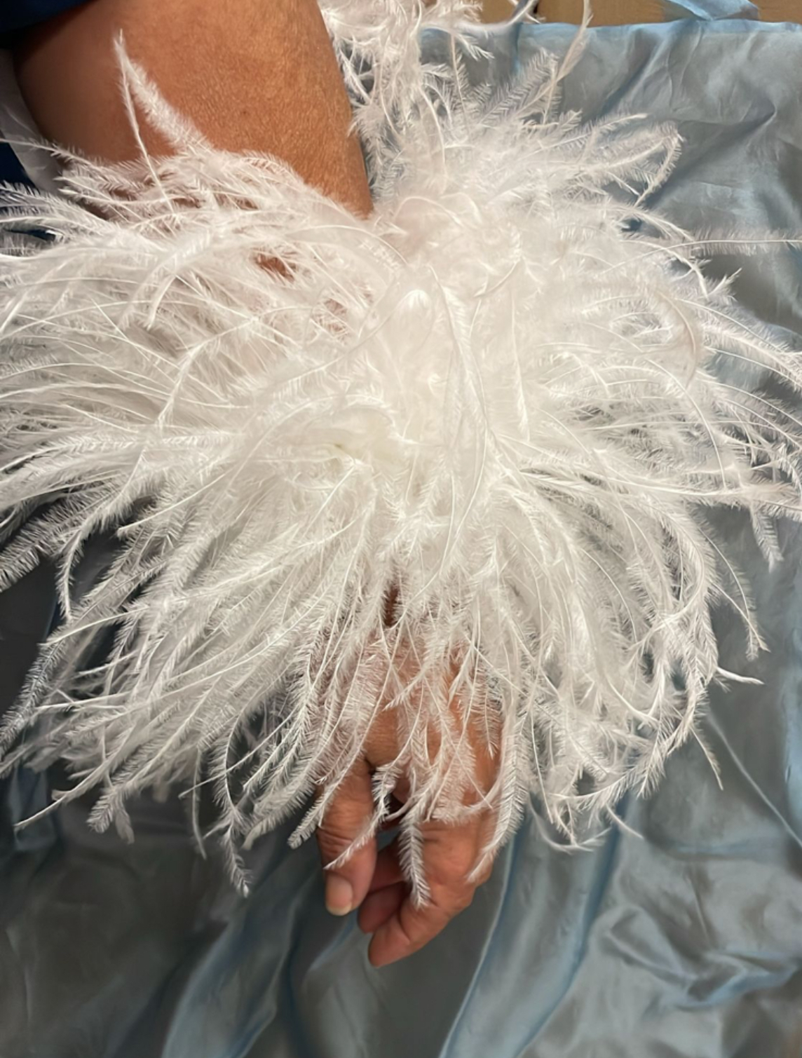 Pareja de puños de plumas de avestruz naturales y desmontables colocados sobre las mangas de un vestido de invitada.